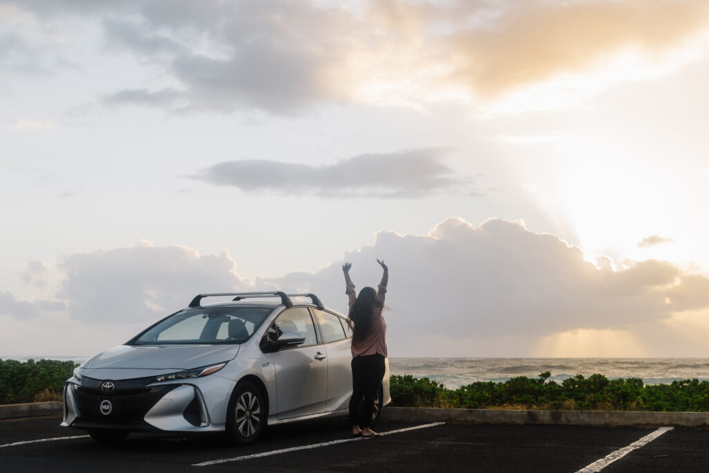 Traveler enjoying a scenic view next to a Hui Car Share vehicle at Sandy Beach on Oahu